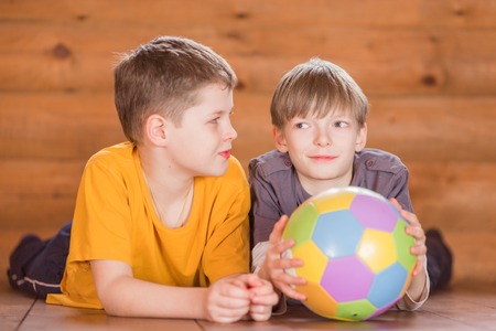Two friends with a ball lying on the wooden floorの写真素材