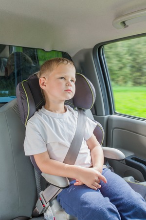 Boy sitting in a car in safety chair fasten by seat beltの写真素材