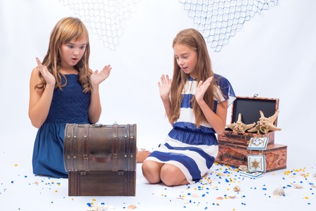 Two beautiful teen girls surprised sitting on the floor near opened chestの写真素材
