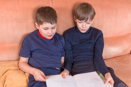 Two boys reading book siiting on the sofaの写真素材