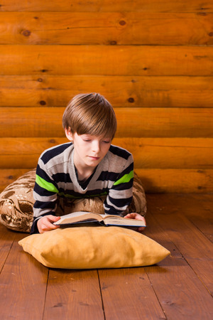 Teenboy reading book lying on wooden floorの写真素材