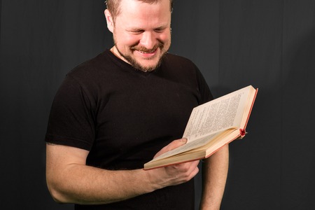 Portrait of middle-aged bearded man reading book on black backgroundの写真素材