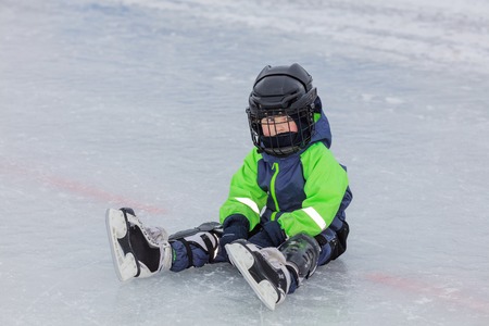 Little boy in skates sitting on ice at outdoor ice rinkの写真素材