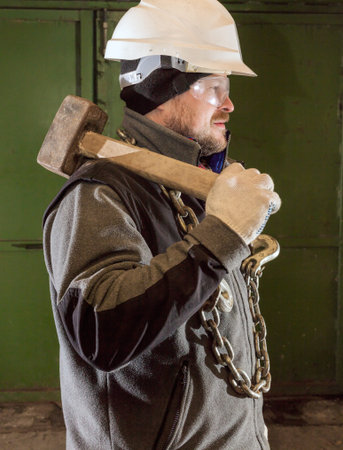 Tough worker in safety helmet with iron chain and sledgehammer