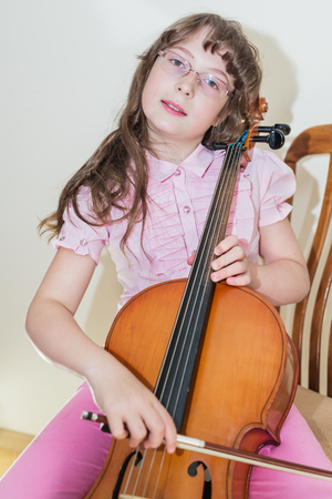 Pretty young girl practice playing cello sitting on chairの写真素材