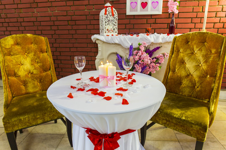 Romantic zone with round table with red petals and burning candlesの写真素材