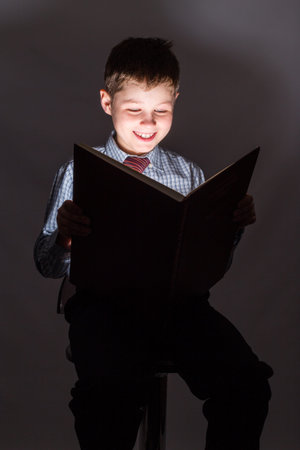 Young schoolboy reading book in the dark on white background