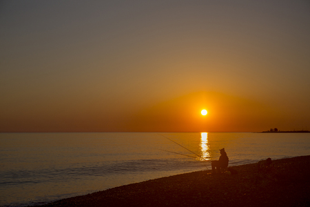 Beautiful scene with fisherman silhouette with rod sitting on sea beachの写真素材