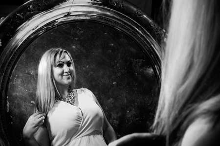 Attractive plump woman looking at her reflection at retro style mirrorの写真素材