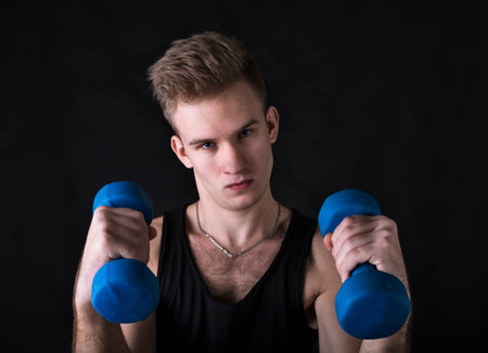 Young sportsman making exercises with dumbbels studio portrait on black background.