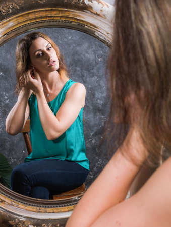 Beautiful young woman looking on her reflection at the mirrorの写真素材