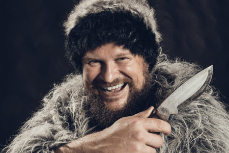 Bearded hunter dressed in a fur mantle and fur hat with knife