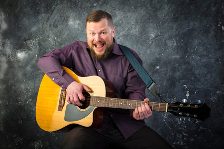 Mature musician plays acoustic guitar emotional studio portrait.