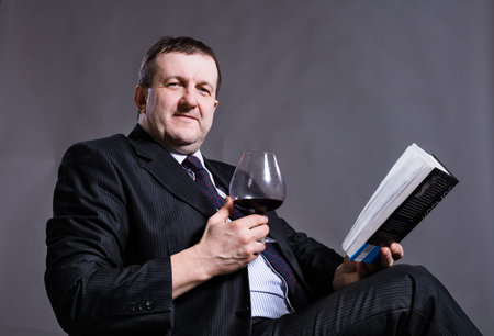 Middle aged solid businessman with glass of wine and book