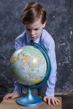 Cute schoolboy dressed in shirt and tie with the globeの写真素材