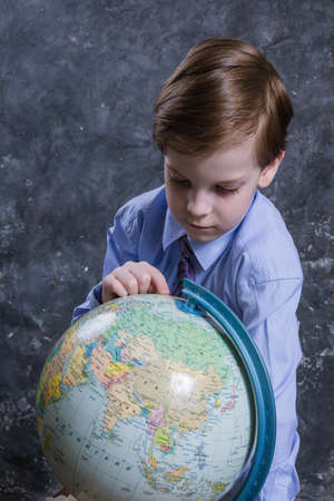 Cute schoolboy dressed in shirt and tie with the globeの写真素材