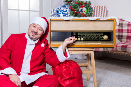 Bearded man dressed in Santa Claus costume sitting close to retro radio setの写真素材