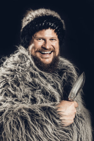 Bearded hunter dressed in a fur mantle and fur hat with knife