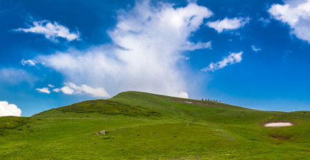 Beautiful mountain landscape at Caucasus mountains with clouds, blue sky and line of horse riders...