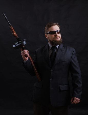 Mature bearded man in sunglasses dressed in suit with tommy gun