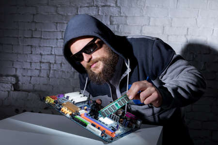 Bearded hacker in sunglasses and hoodie cracking the hardwareの写真素材
