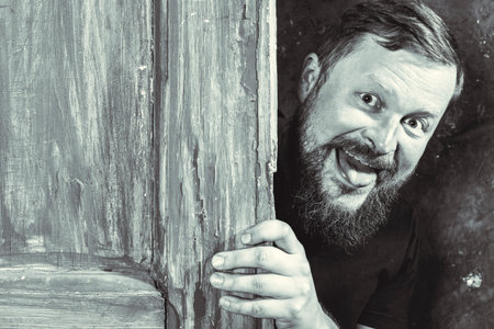 Cheerful bearded man peering out of the doorの写真素材