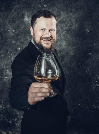 Solid smiling bearded man in suit with glass of whiskyの写真素材