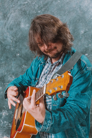 Mature musician plays acoustic guitar studio portrait.