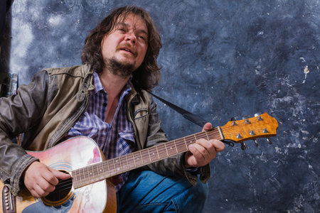 Mature musician plays acoustic guitar studio portrait.