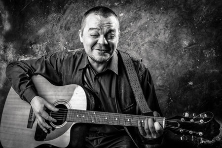 Mature musician plays acoustic guitar emotional studio portrait.