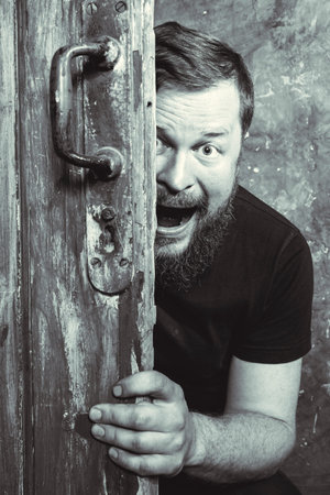 Cheerful bearded man peering out of the door
