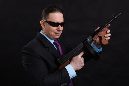 Mature gangster in sunglasses dressed in suit with tommy gun