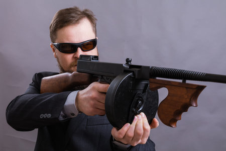 Mature man in sunglasses dressed in suit with tommy gun