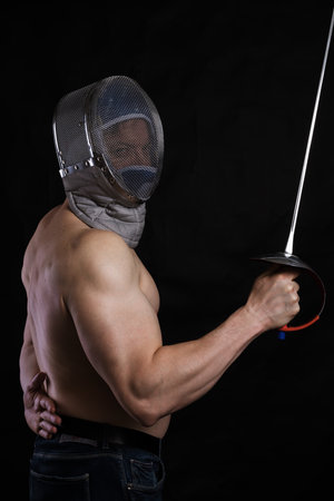 Matured man with   muscular torso in fencing helmet and epeeの写真素材