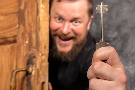 Cheerful bearded man with key peering out of the doorの写真素材