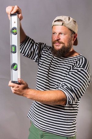 Joyful bearded craftsman with level and blanc cube studio portrait
