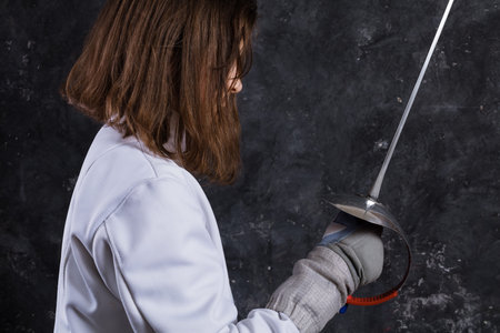 Teenage girl fencer dressed in uniform with epee and helmet