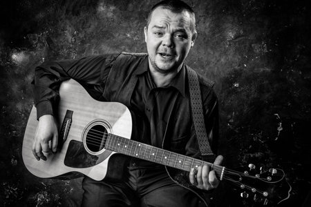Mature musician plays acoustic guitar emotional studio portrait.
