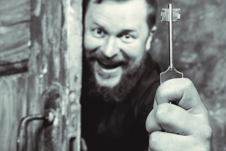 Cheerful bearded man with key peering out of the door