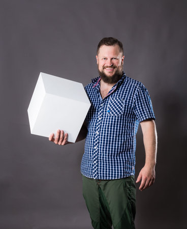 Joyful bearded man in shirt with blanc object looks like cube