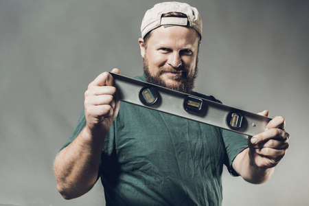 Joyful bearded craftsman in green t-shirt with level toolの写真素材
