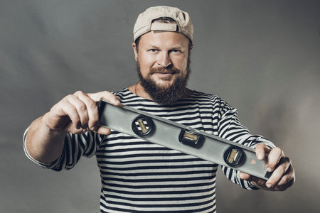 Joyful bearded craftsman with level and blanc cube studio portraitの写真素材