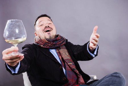 Solid cheerful man in kerchief sitting with glass of wineの写真素材