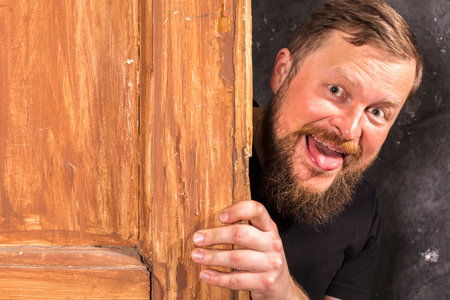 Cheerful bearded man peering out of the doorの写真素材
