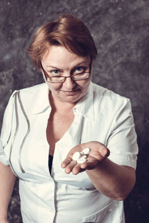 Middle aged woman pharmacist in medical robe offers the tabletsの写真素材