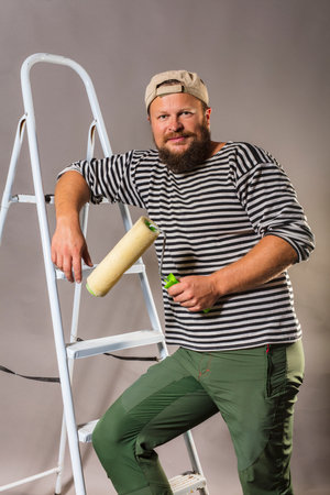 Joyful bearded craftsman with brush roller and ladderの写真素材