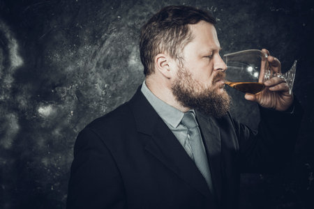 Solid bearded man in suit tasting whisky in a glassの写真素材