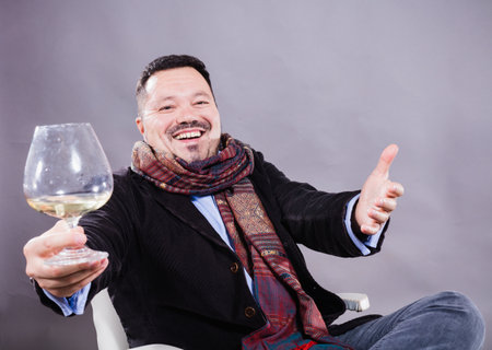 Solid cheerful man in kerchief sitting with glass of wineの写真素材