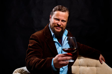 Stylish bearded man dressed in brown jacket with glass of whiskyの写真素材
