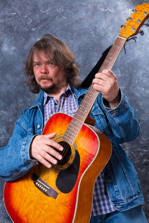 Mature musician plays acoustic guitar studio portrait.の写真素材